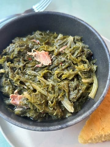 A bowl filled with southern mustard greens and a piece of cornbread on the side.