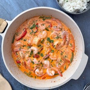 A cream-colored pan filled with spicy shrimp curry, with a bowl of white rice on the side.