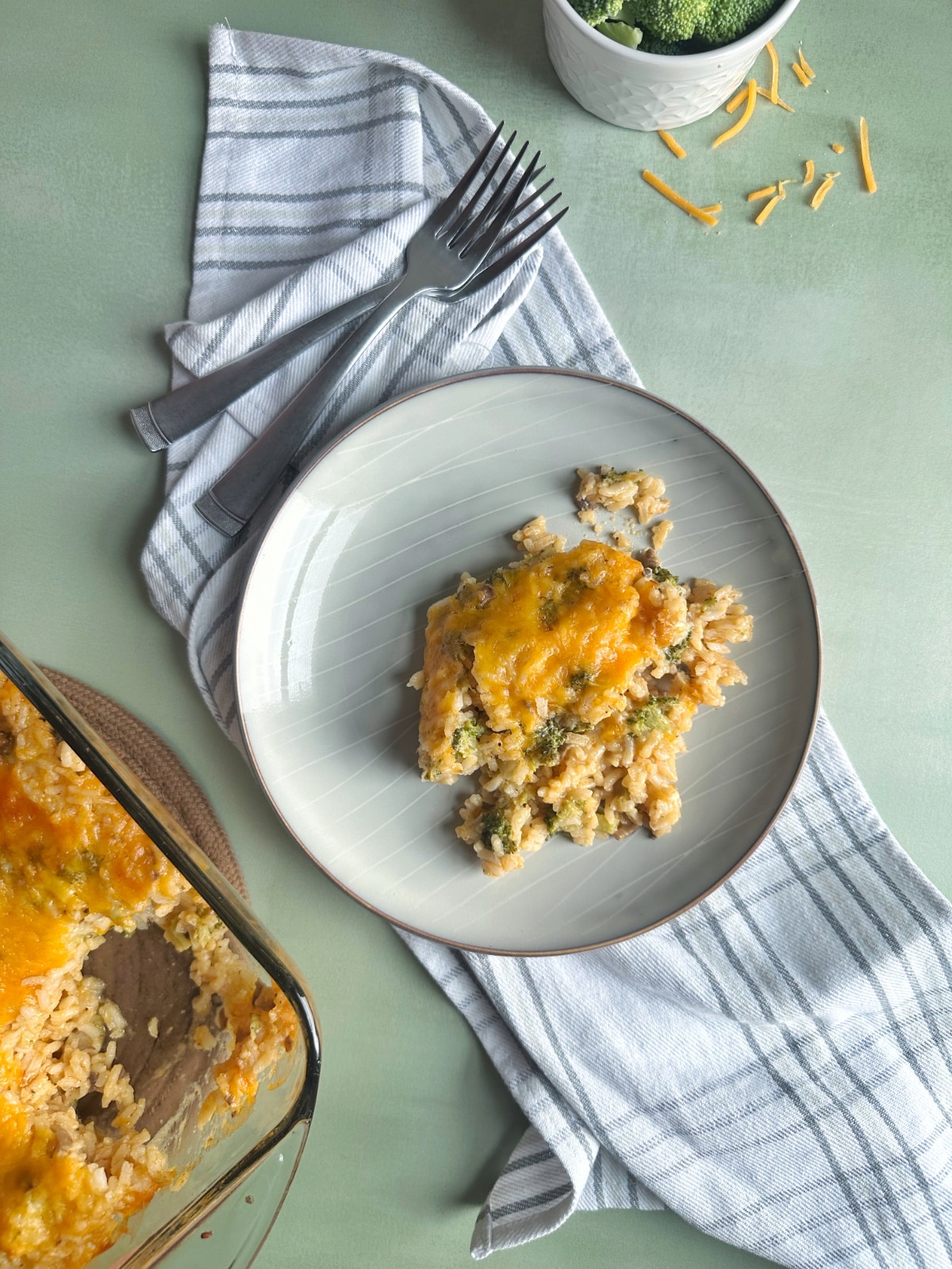 A plate of broccoli rice casserole, with the pan, extra broccoli, and two forks on the side.