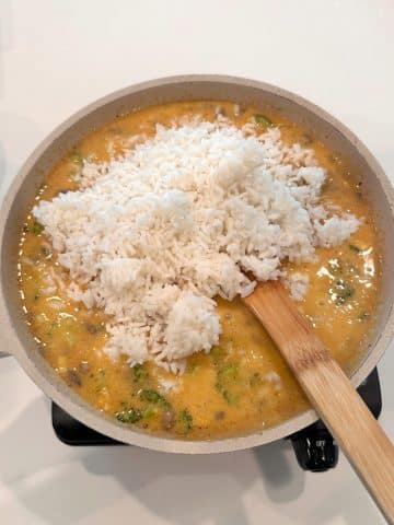 Cooked rice being added to a broccoli cheddar casserole base sauce.