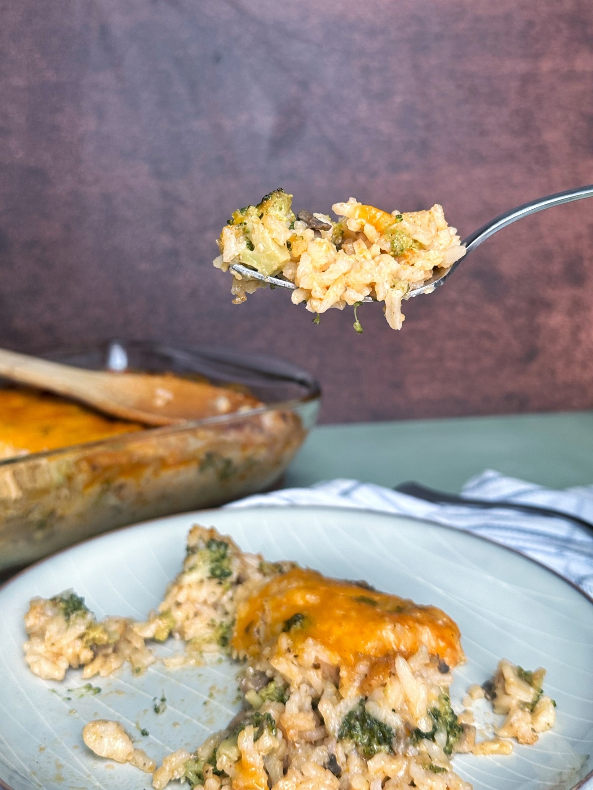 A fork holding up a biteful of broccoli rice casserole over the rest of the plate.
