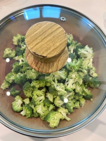Freshly chopped broccoli being steamed in a cream colored pot.