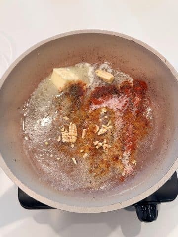 Dry spices being toasted in a pan of melted butter.