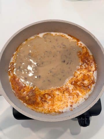 Milk, seasonings, and cream of mushroom soup cooking in a tan-colored pan.