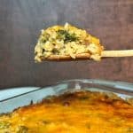 A wooden spoon holding up a scoop of broccoli rice casserole over the rest of the pan.