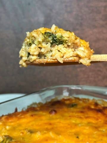 A wooden spoon holding up a scoop of broccoli rice casserole over the rest of the pan.