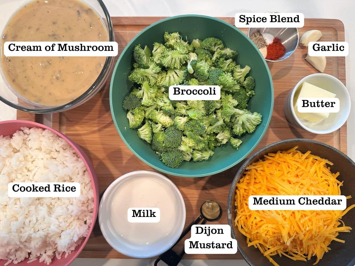 A wooden board containing ingredients for cheddar broccoli rice casserole, including cheese, cooked rice, and cream of mushroom soup.