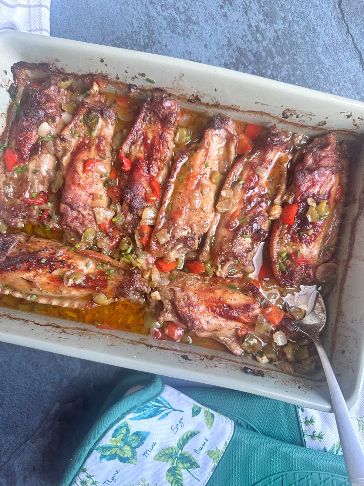 A pan of baked turkey wings with peppers and onions on top.