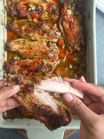 A hand pulling apart a baked turkey wing to show the texture of the meat.