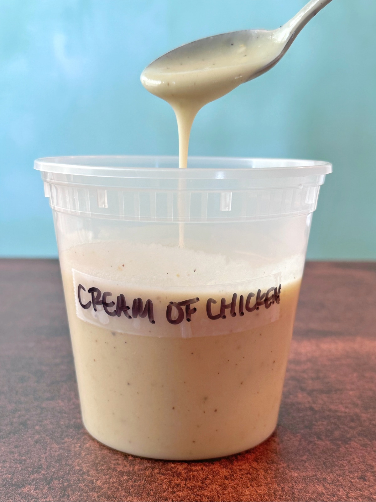 A spoon pouring cream of chicken soup back into its plastic deli container.