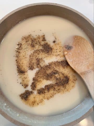 A saucepan filled with a white cream sauce and dry spices poured on top.