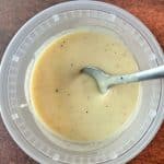 A plastic deli container filled with homemade cream of chicken soup with a spoon in the middle.