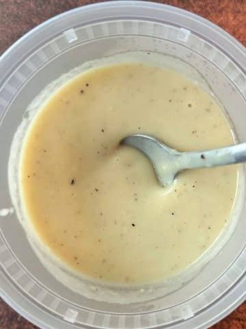 A plastic deli container filled with homemade cream of chicken soup with a spoon in the middle.