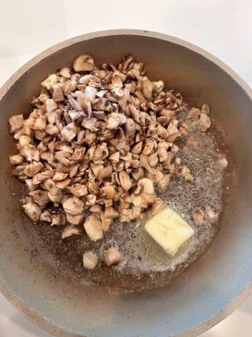 A pan with chopped mushrooms sautéing in melted butter.