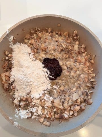 A pan of sautéed mushrooms, a dark brown vegetable bouillon, and flour.