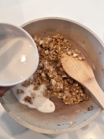 A bowl of milk being poured into a pan of roux-covered mushrooms.