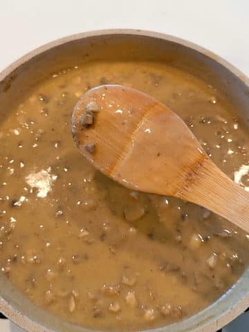 The back of a wooden spoon covered with homemade cream of mushroom soup.