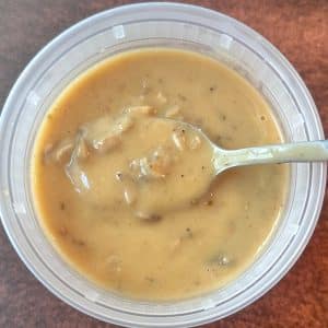A plastic deli container filled with homemade cream of mushroom soup with a spoon in the middle.