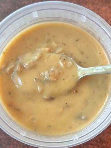 A plastic deli container filled with homemade cream of mushroom soup with a spoon in the middle.
