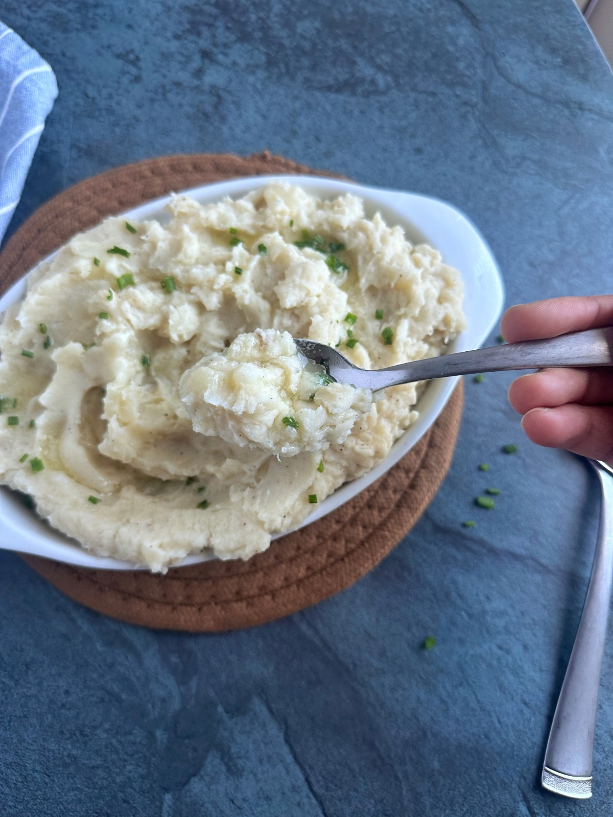 A hand holding a spoonful of mashed potatoes over the rest of the dish.