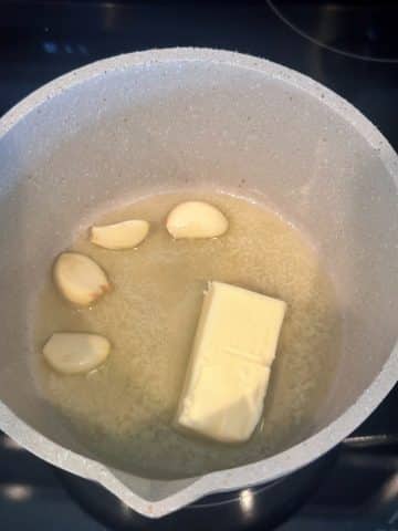 A saucepan with melted butter and fresh garlic cloves.