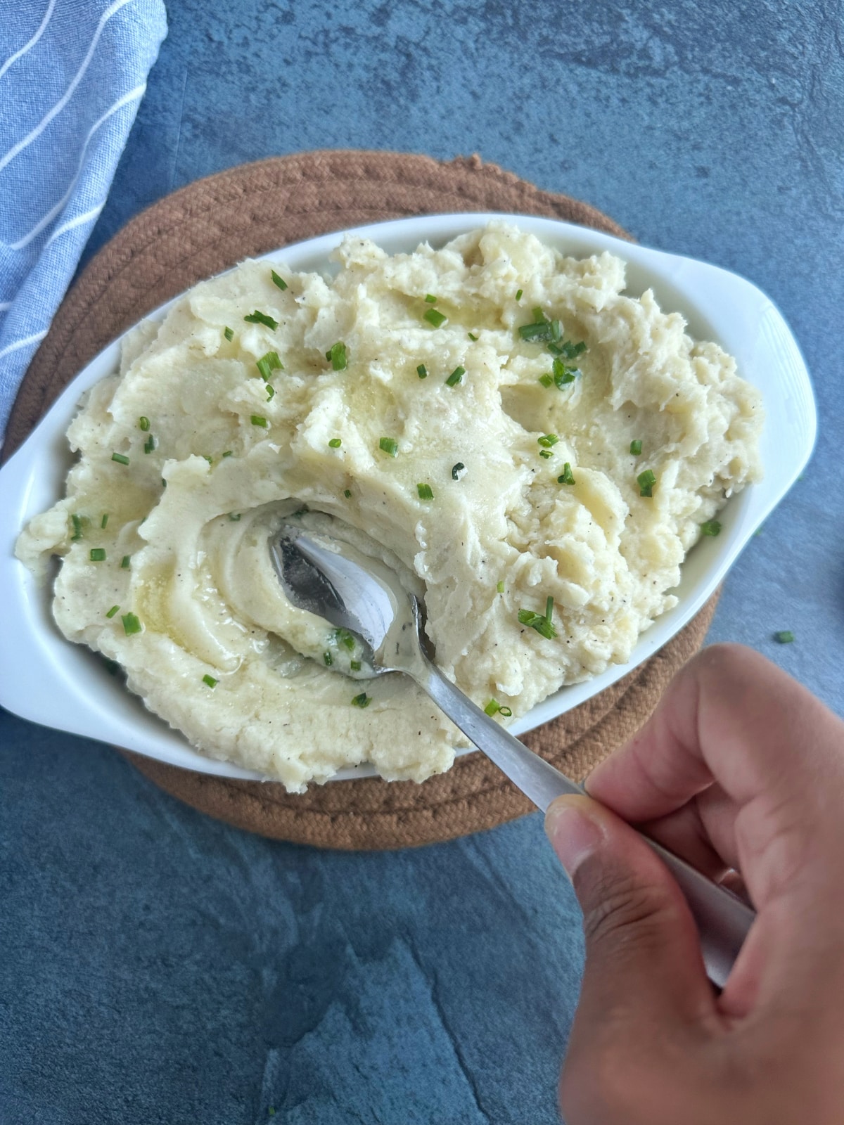 A spoon stirring into a white ceramic dish filled with mashed potatoes.