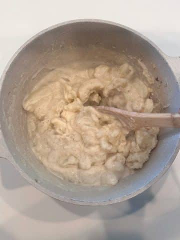 A wooden spoon stirring mashed potatoes in a large, cream colored pot.
