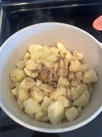 A large pan filled with chopped, boiled potatoes and seasonings on top.