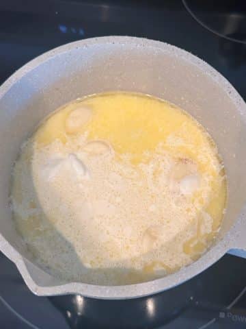 A saucepan with melted butter, cream, milk, and fresh garlic cloves.