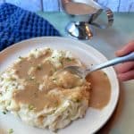 A plate of mashed potatoes with homemade gravy poured on top.