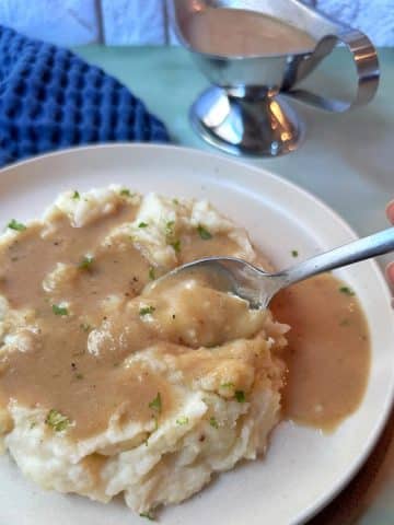 A plate of mashed potatoes with homemade gravy poured on top.