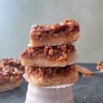 A stack of three salted caramel pecan bars on a white ceramic stand.