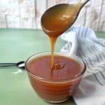 A spoon pouring a drizzle of salted caramel sauce into a glass bowl.