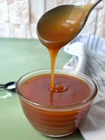 A spoon pouring a drizzle of salted caramel sauce into a glass bowl.