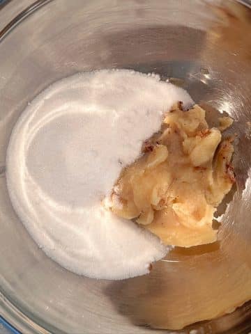 A mixing bowl with granulated sugar and cooled brown butter inside.