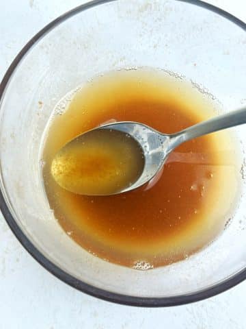A clear bowl filled with browned butter, with a spoon stuck in the center.
