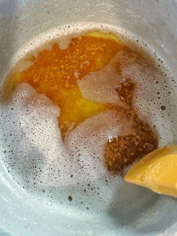 A silicone spatula pulling back a layer of foam to show the browned butter underneath.