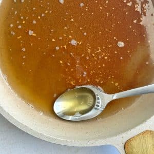 A spoonful of browned butter sitting in a pan filled with the rest of the liquid.