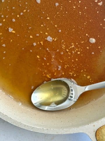 A spoonful of browned butter sitting in a pan filled with the rest of the liquid.