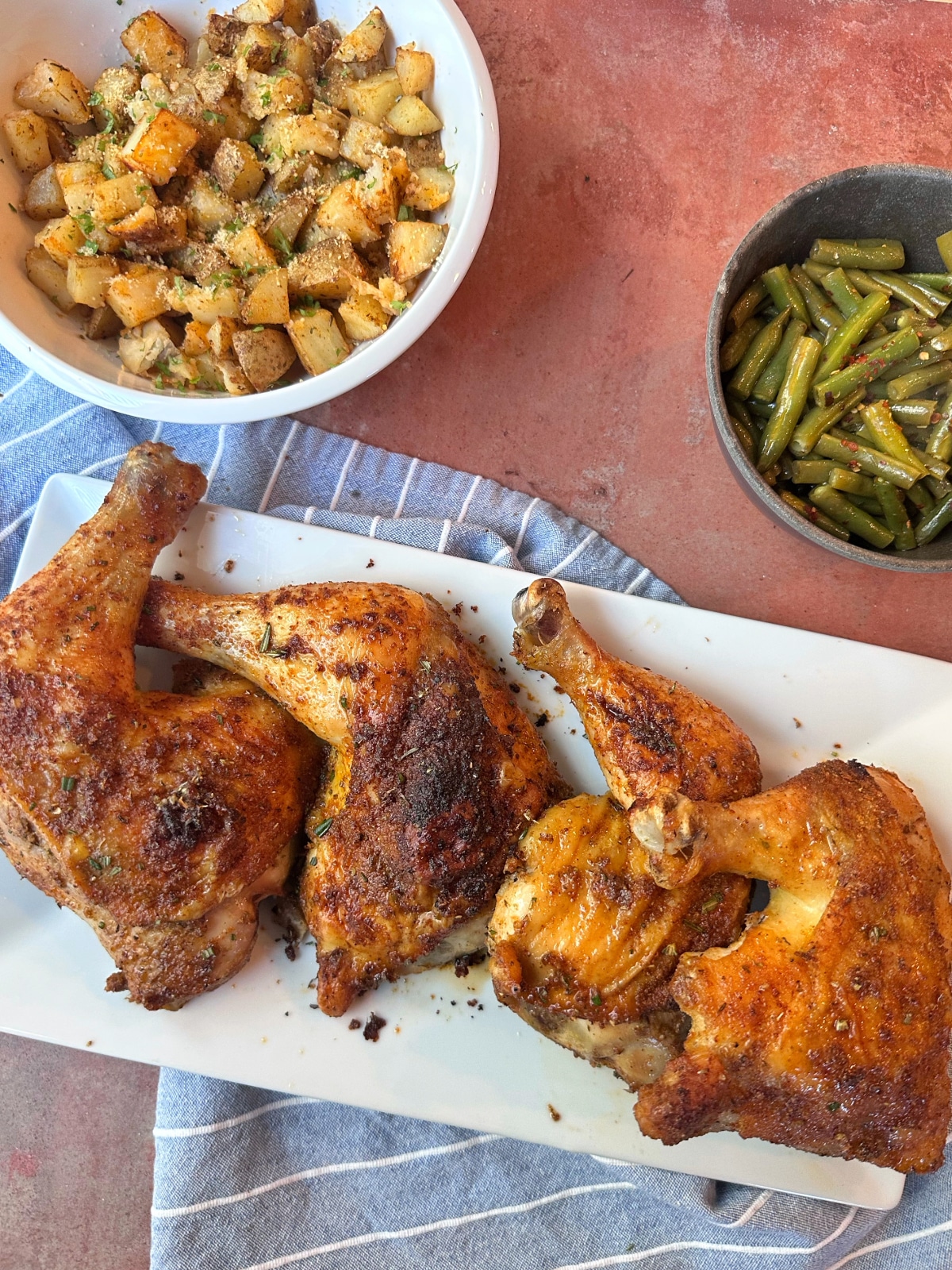 Roasted Chicken Quarters on a white plate with potatoes and green beans on the side.