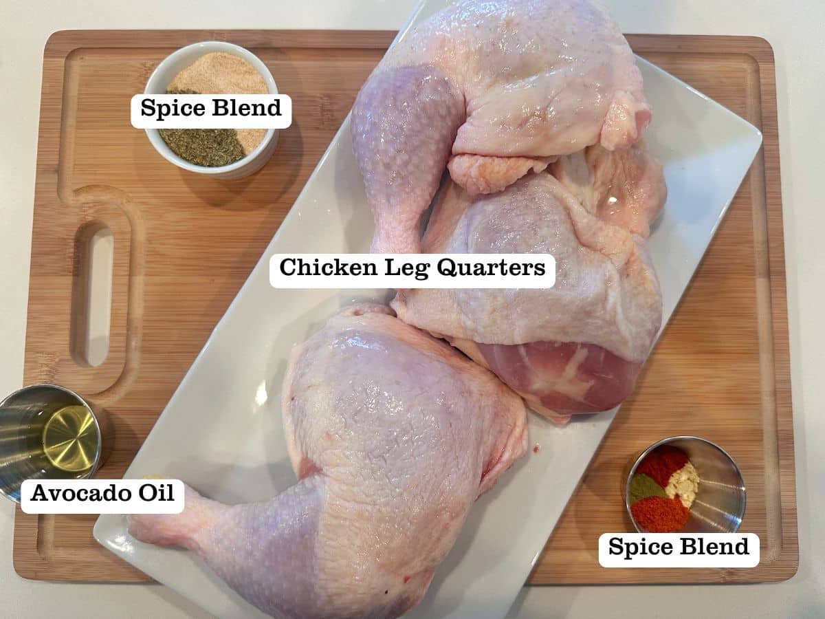 A wooden board containing raw chicken leg quarters on a white plate, along with bowls of oil and seasonings.
