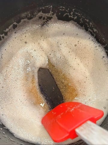 A saucepan filled with browned butter, with a silicone spatula parting through the liquid.