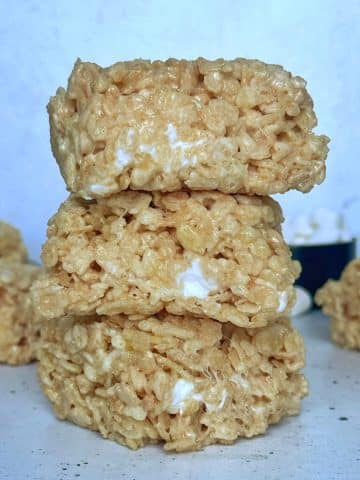 A stack of 3 Brown Butter Rice Krispie treats on a white countertop with more treats in the back.
