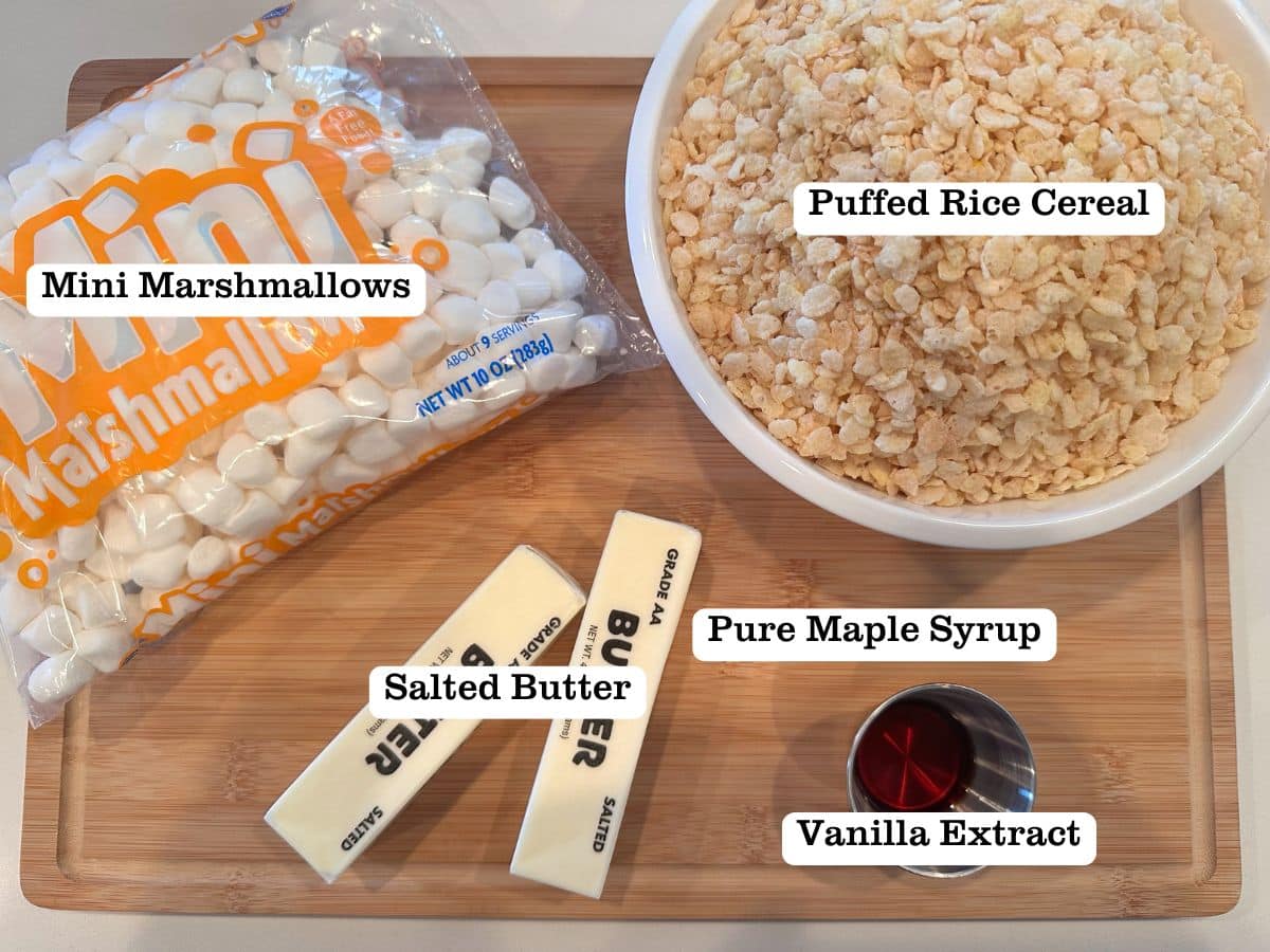 A wooden board containing ingredients for homemade cereal treats, including butter, marshmallows, and puffed rice cereal.