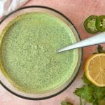 A bowl of green goddess dressing with a spoon sticking out of it.