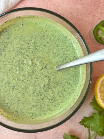 A bowl of green goddess dressing with a spoon sticking out of it.