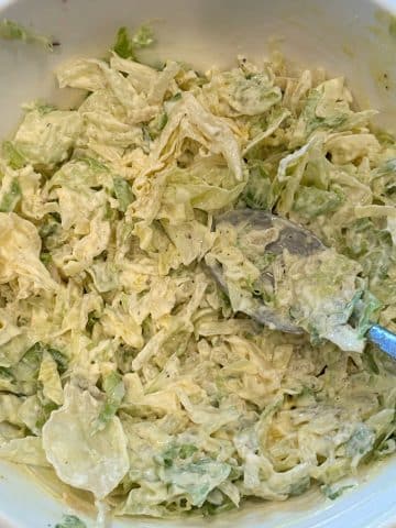 A bowl filled with romaine lettuce coleslaw with a spoon sticking out of it.