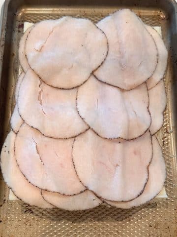 Layers of deli meat on top of cheese and a row of bottom slider buns.