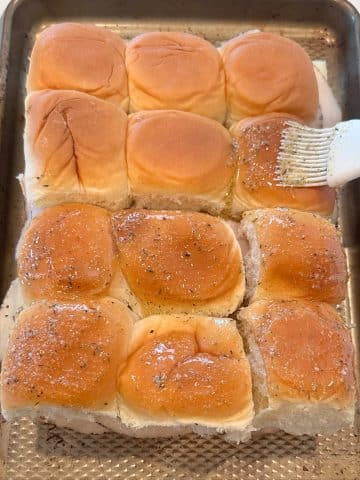 Garlic butter being brushed onto dinner rolls.