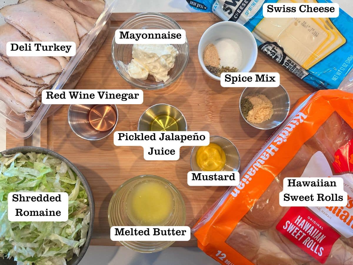 A wooden board containing ingredients for turkey and cheese sliders, including lettuce, sweet rolls, and melted butter.